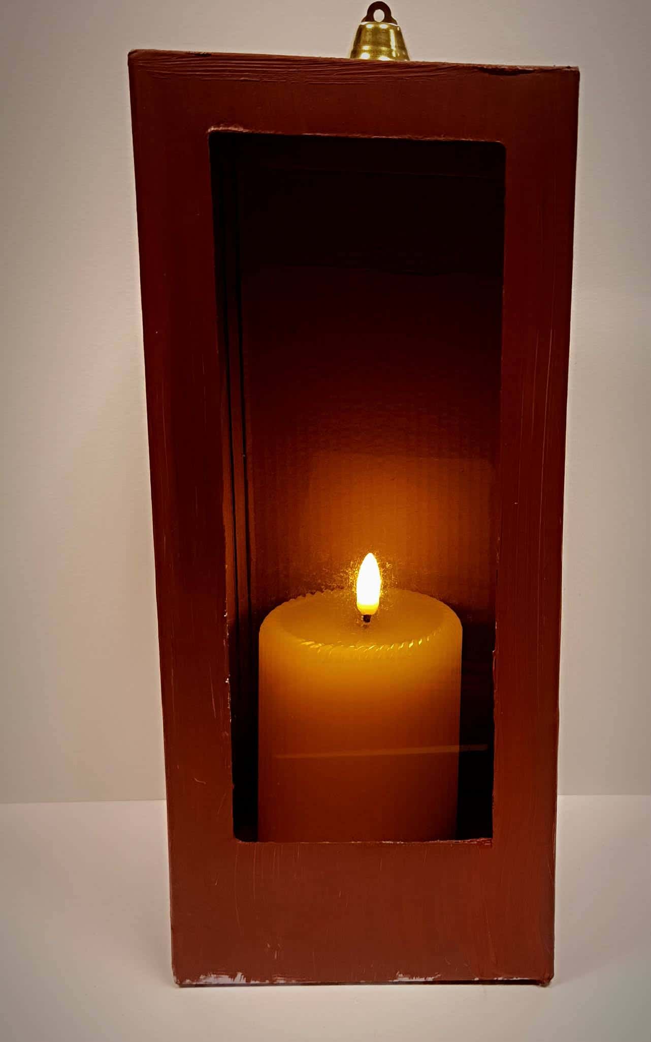 Brązowy lampion z kartonu z wyciętym okienkiem i zapaloną świecą w środku – praca dziecka.