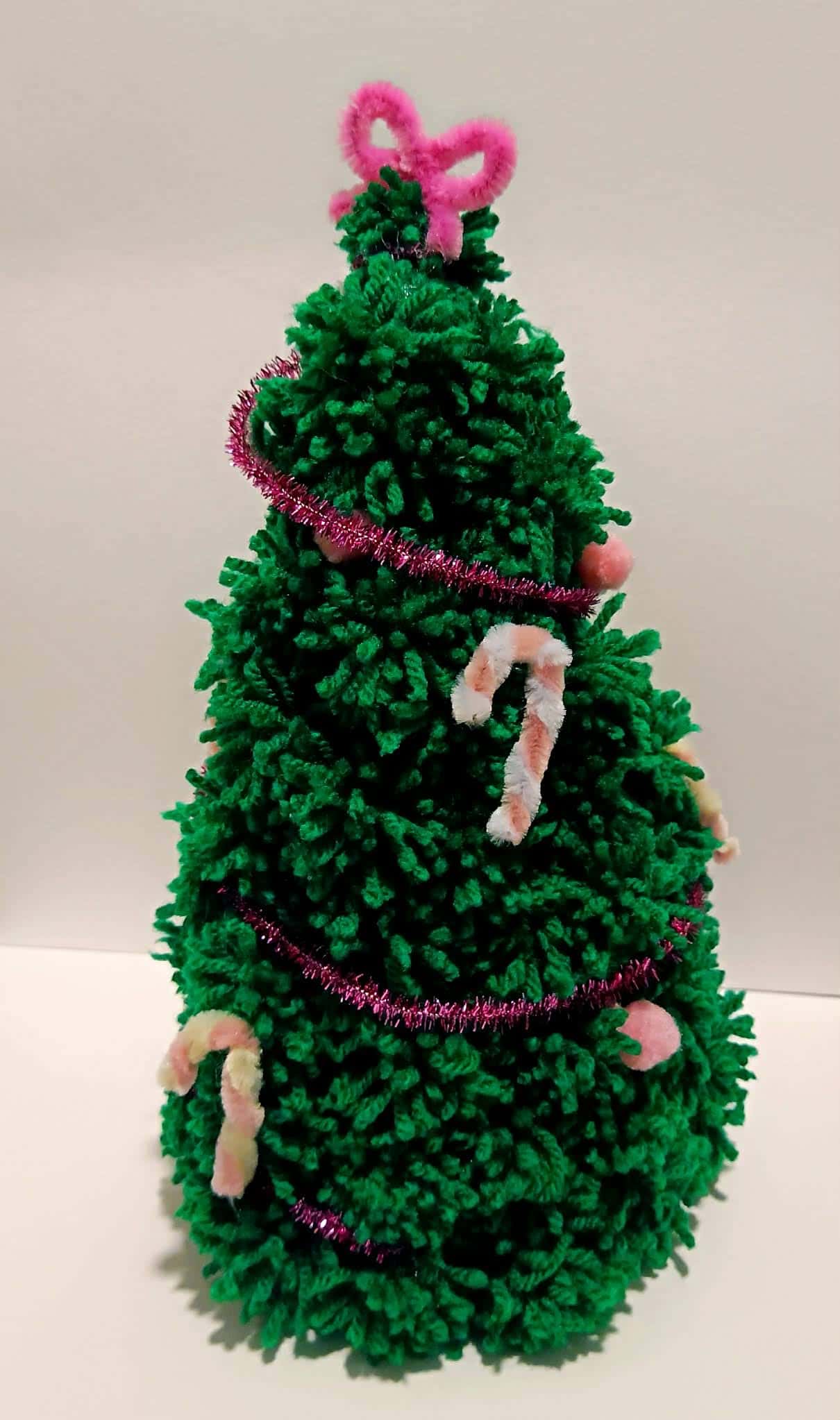 Zielona choinka z włóczki ozdobiona różowym łańcuchem i małymi cukrowymi laskami – praca dziecka.